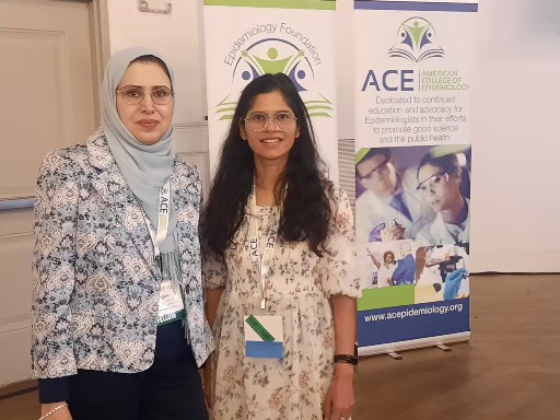 A woman with glasses and a head scarf poses with a woman with dark hair and glasses both smiling at the camera