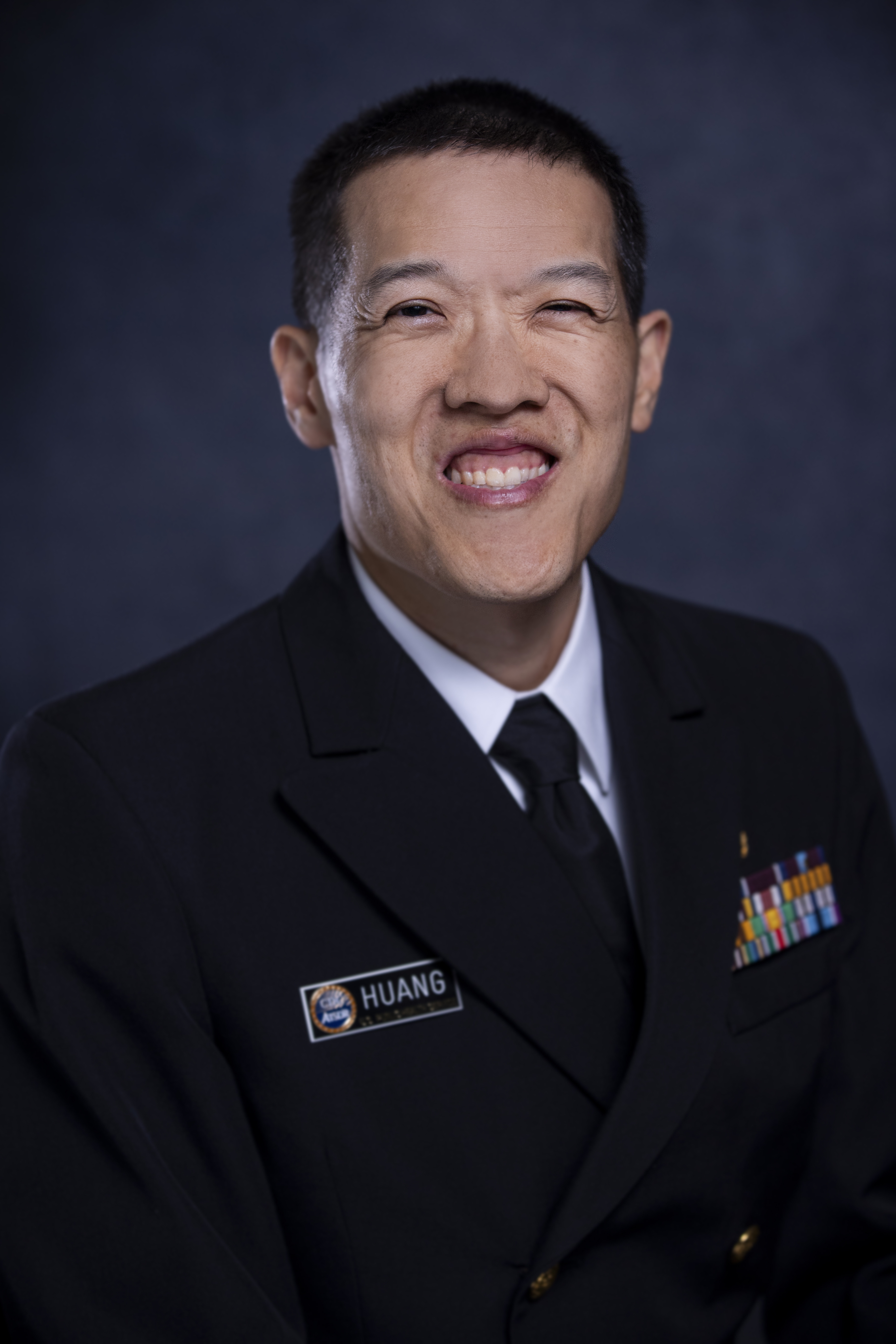 An Asian man with shrot cropped hair in military dress smiles wide at the camera