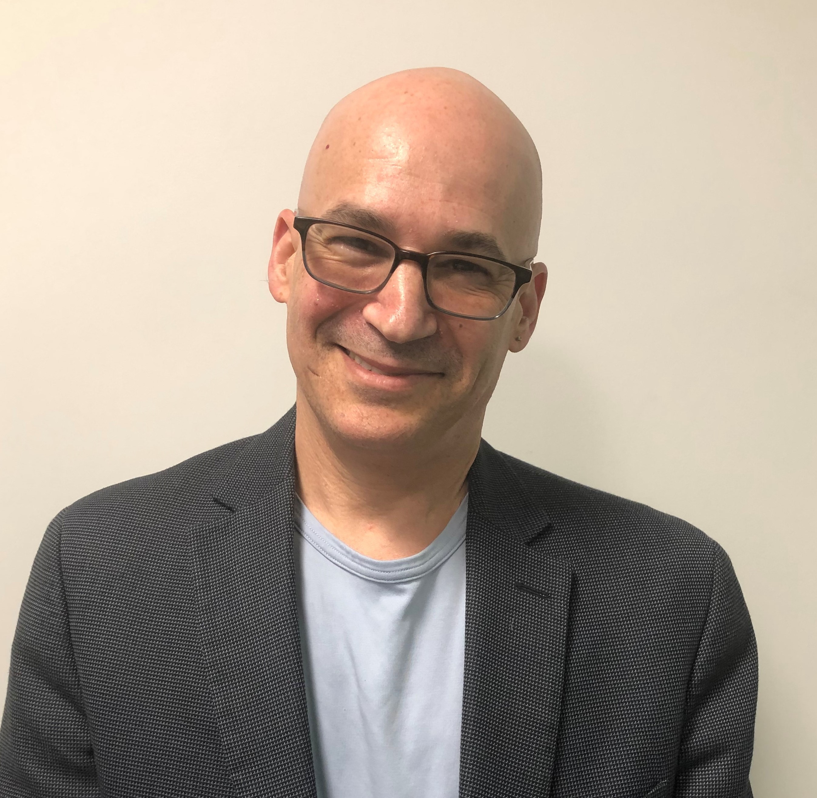 A white bald man with glasses smiling warmly