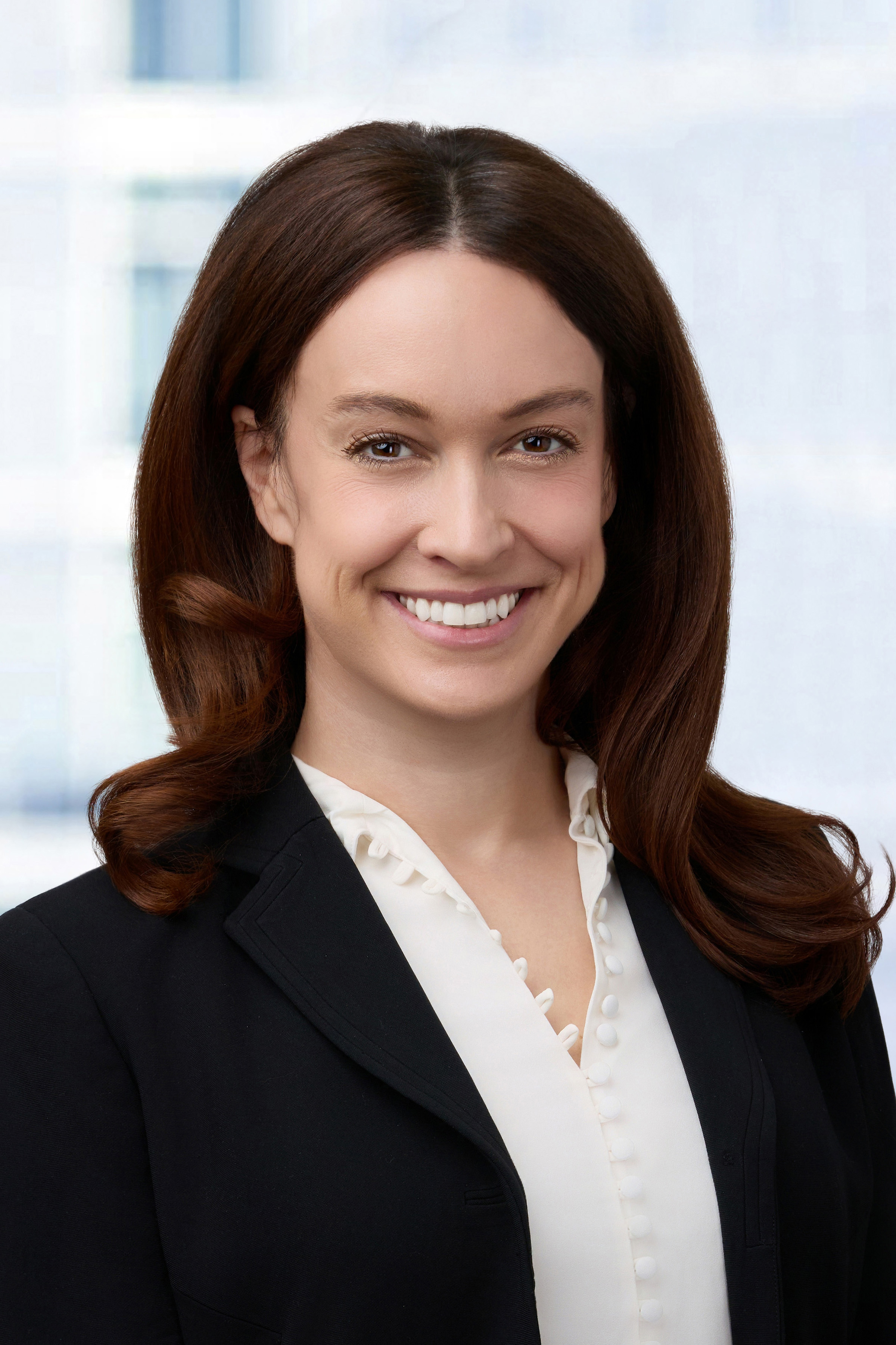 A woman in professional dress and long brown hair smiles at the camera