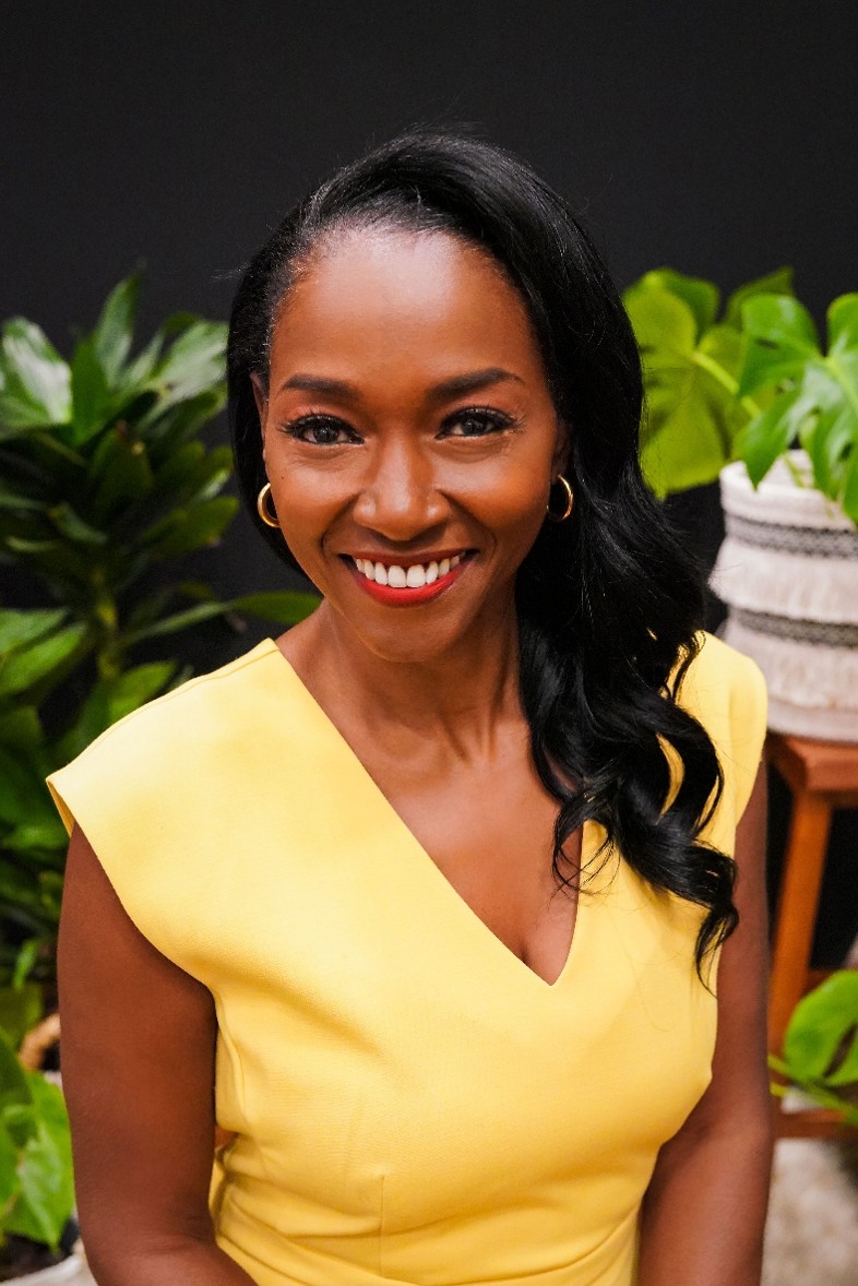 A dark skined woman in a yellow dress smiles at the camera