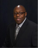 A black man with glasses in professional dress posing for the camera