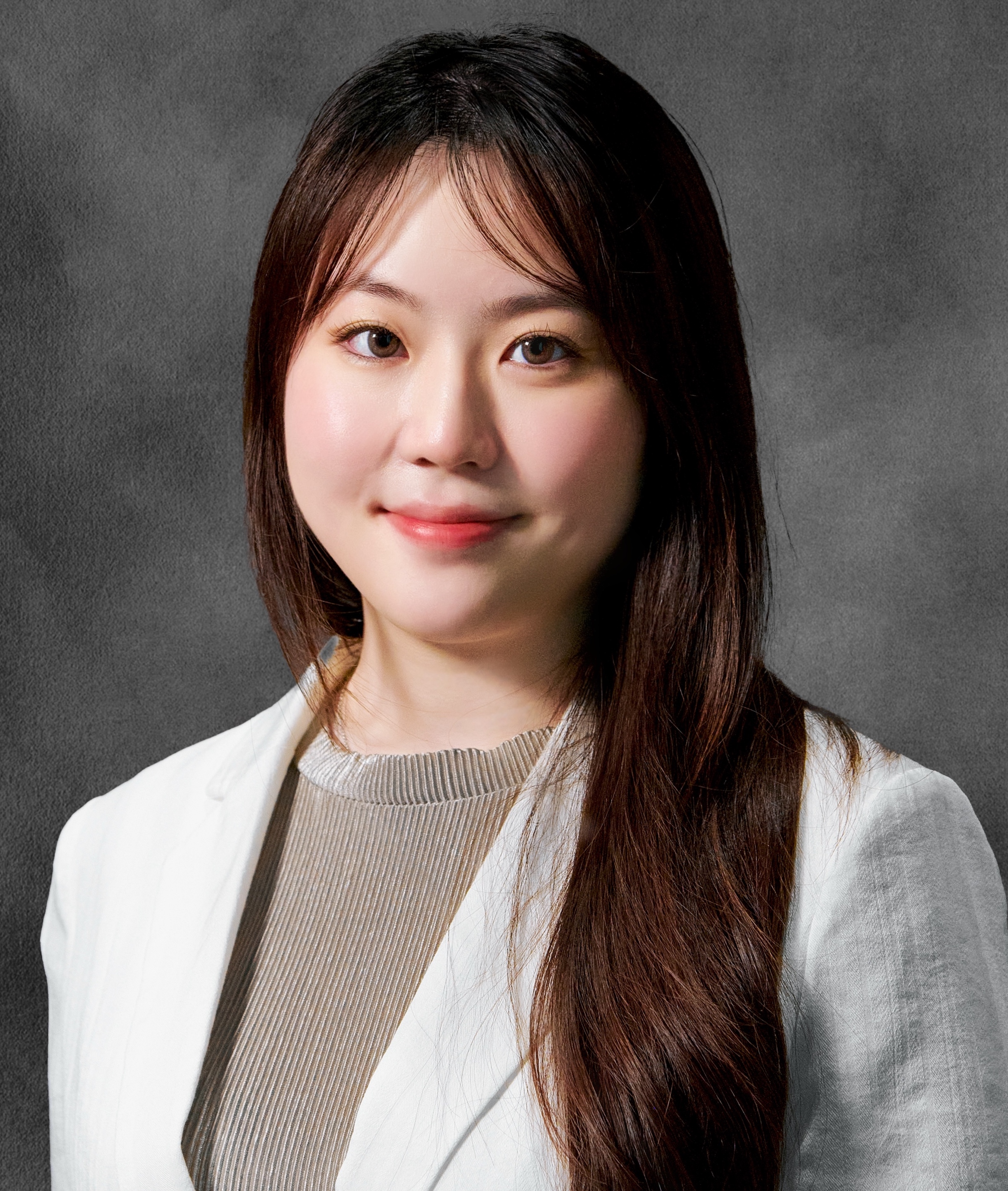 An Asian woman in a white jacket with long dark hair and  brown eyes smiles